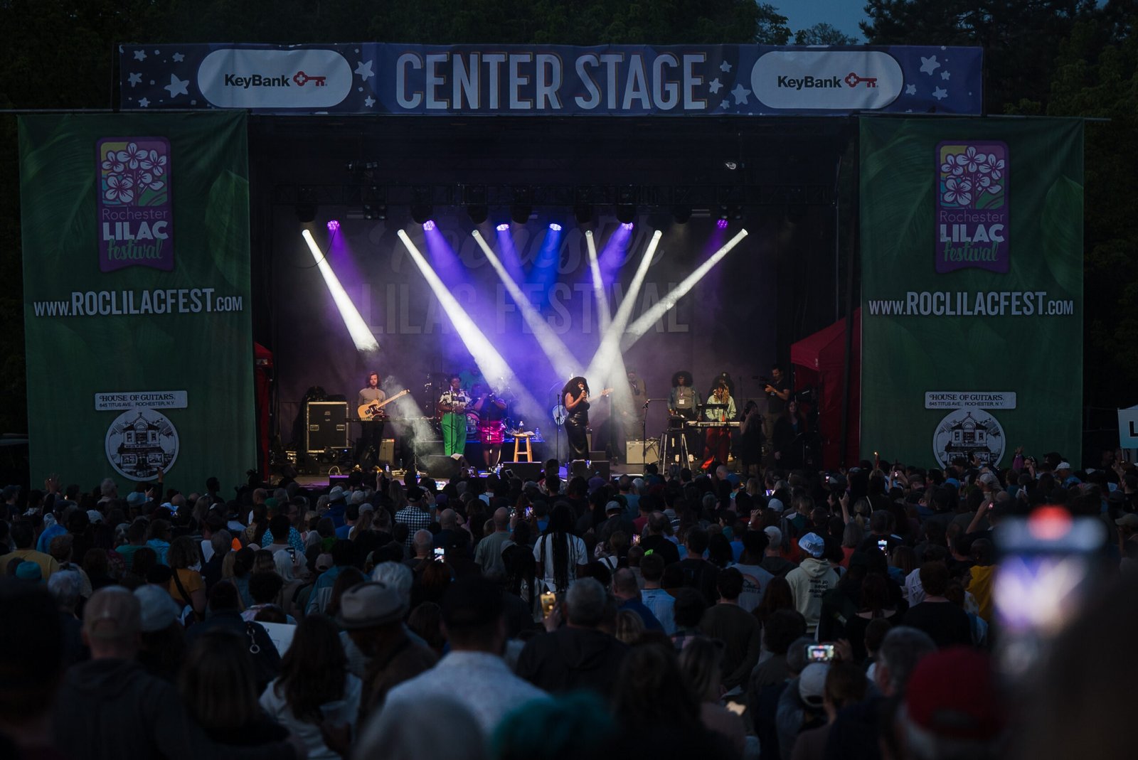 A band performs on the KeyBank Center Stage at night with concert lighting and a packed crowd at the Rochester Lilac Festival