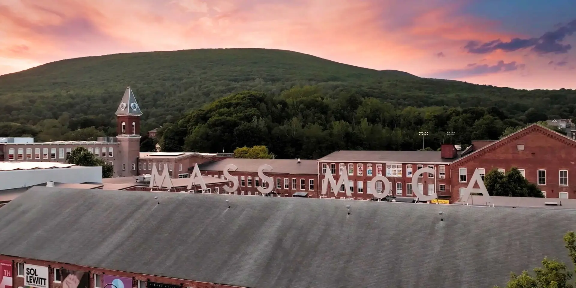 MASS MoCA exterior campus aerial view with converted brick factory buildings and Berkshire mountains at sunset in North Adams Massachusetts
