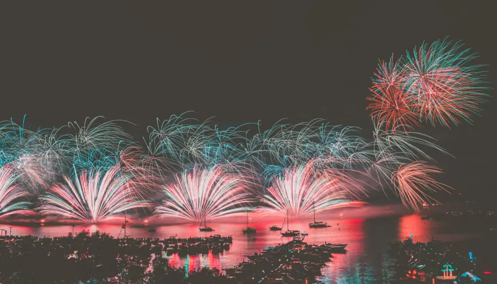 Fireworks display over Oswego Harbor with boats and crowd along the waterfront
