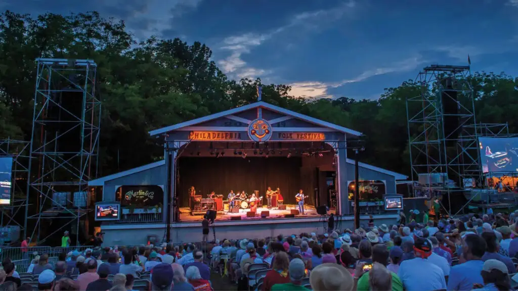 Philadelphia Folk Festival main stage at dusk with performers and seated audience at Old Pool Farm
