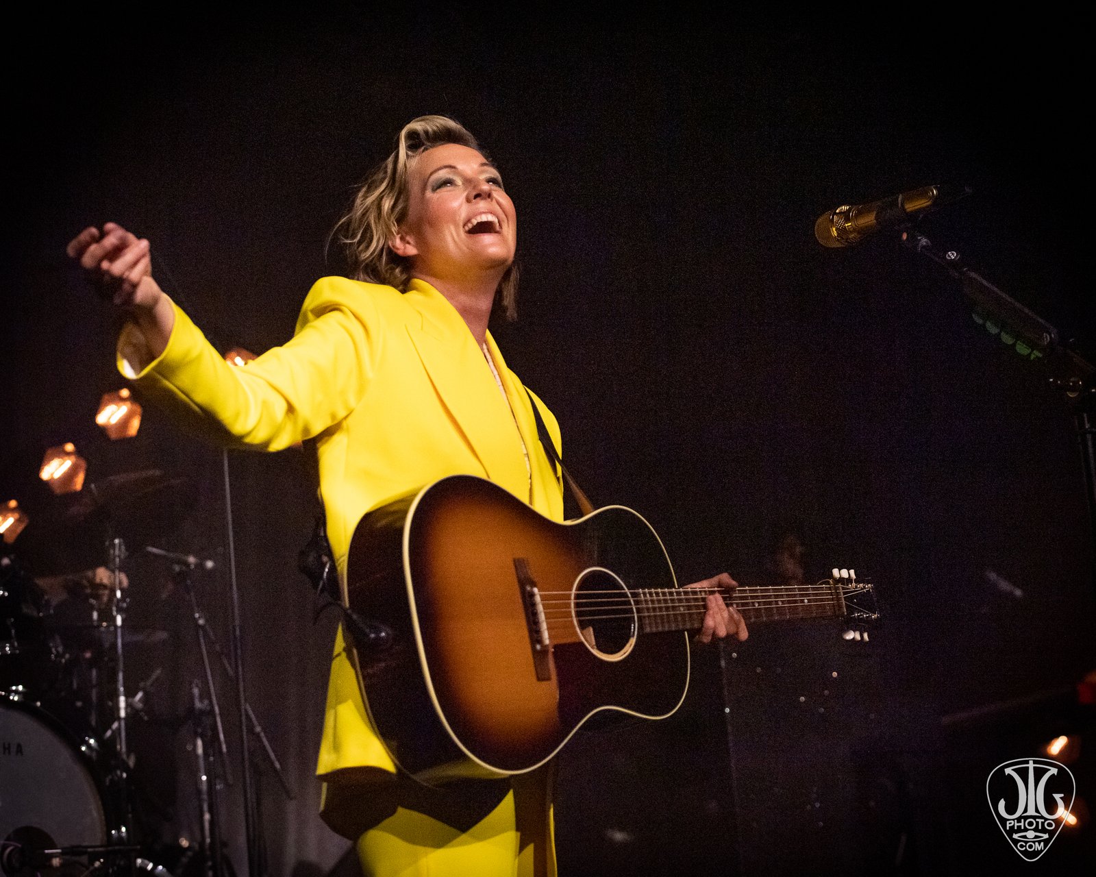 Brandi Carlile performing in a yellow suit, arms outstretched with guitar
