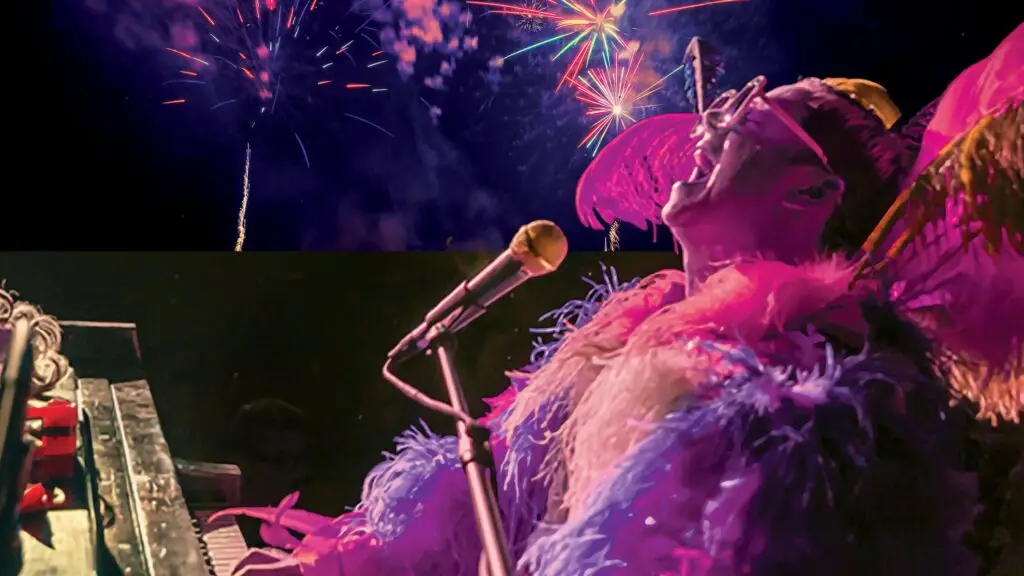 The Rocket Man Show performer in elaborate feathered Elton John costume at piano with fireworks