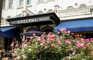 The Adelphi Hotel exterior on Broadway in Saratoga Springs, with colorful flowers in the foreground