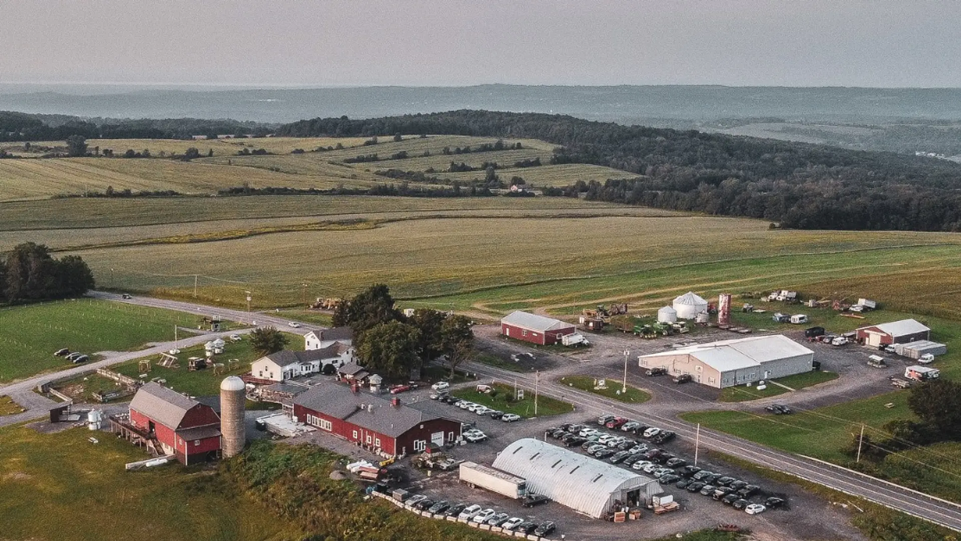Aerial view of Heritage Hill Brewhouse farm in Pompey NY — red barn, silo, brewery, and rolling Central New York fields at dusk