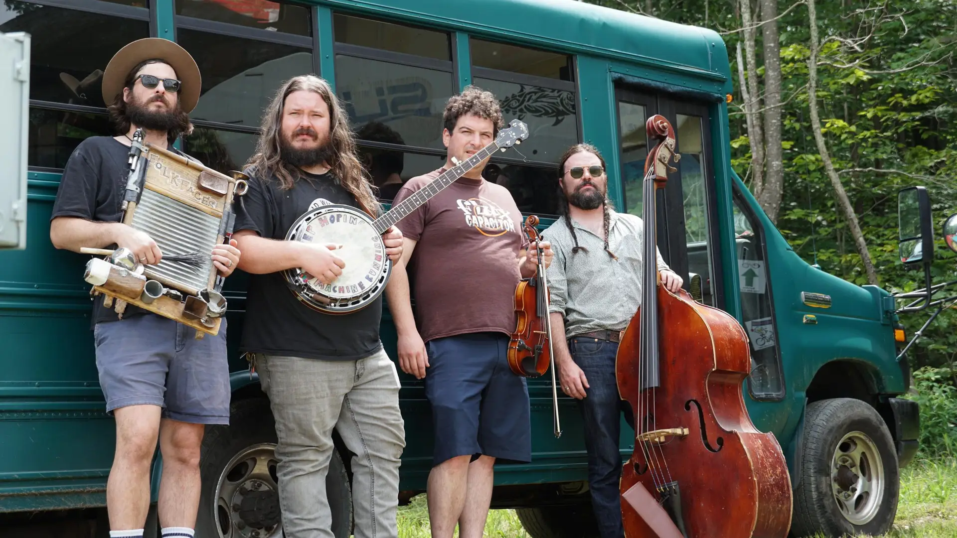 FolkFaces quartet with washboard, banjo, fiddle and upright bass posing in front of their tour bus