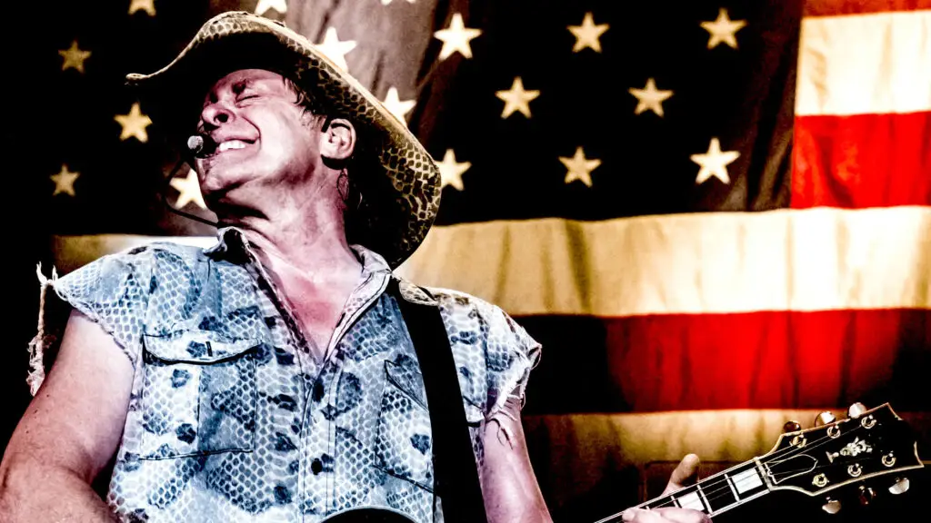 Ted Nugent performing live with guitar in front of American flag backdrop
