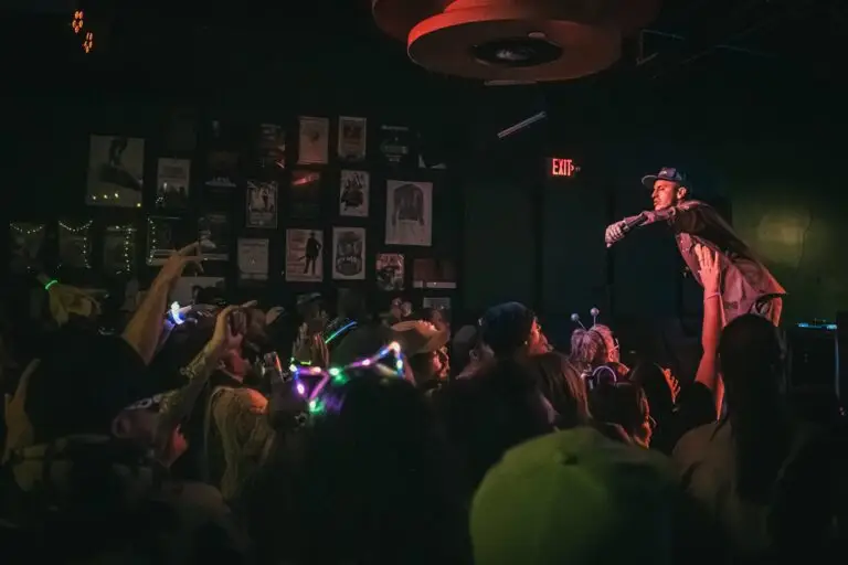 Wax performs live on stage at an intimate venue, leaning into the crowd with microphone