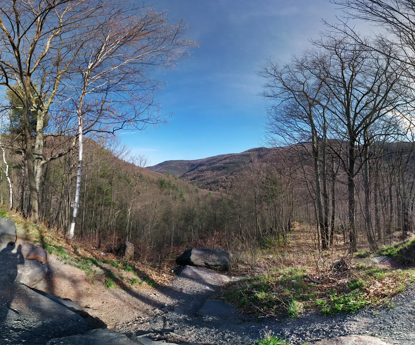Panoramic view of Kaaterskill Clove in the Catskill Mountains of Greene County, New York — wooded ridgelines, mountain terrain falling into a deep valley, blue sky with scattered clouds.