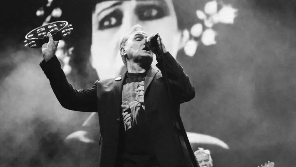Morrissey performs live, holding a tambourine and singing into a microphone on stage