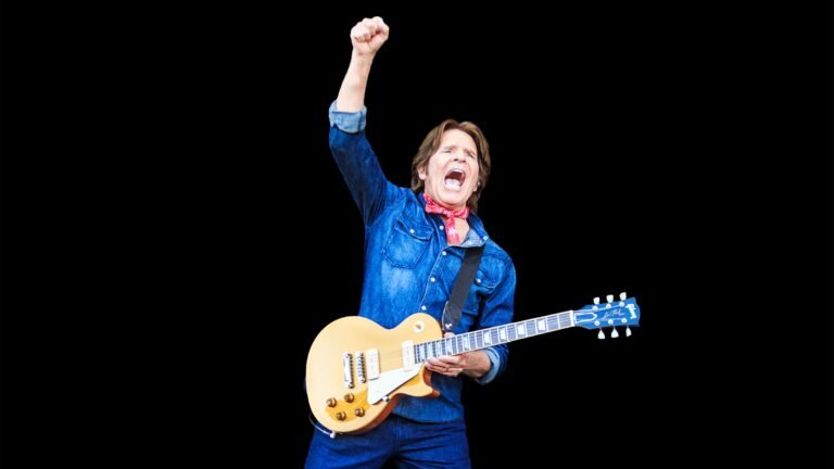 John Fogerty performs with Gibson Les Paul guitar, fist raised — Legacy Tour 2026 promotional photo