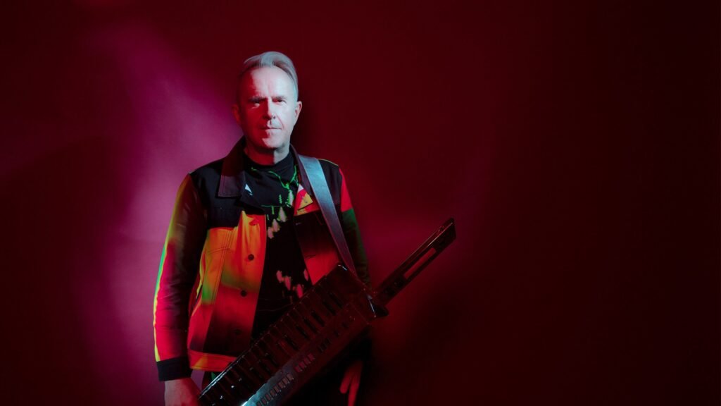 Howard Jones holds a keytar in a promotional photo for his 2026 Things Can Only Get Better Tour at Artpark