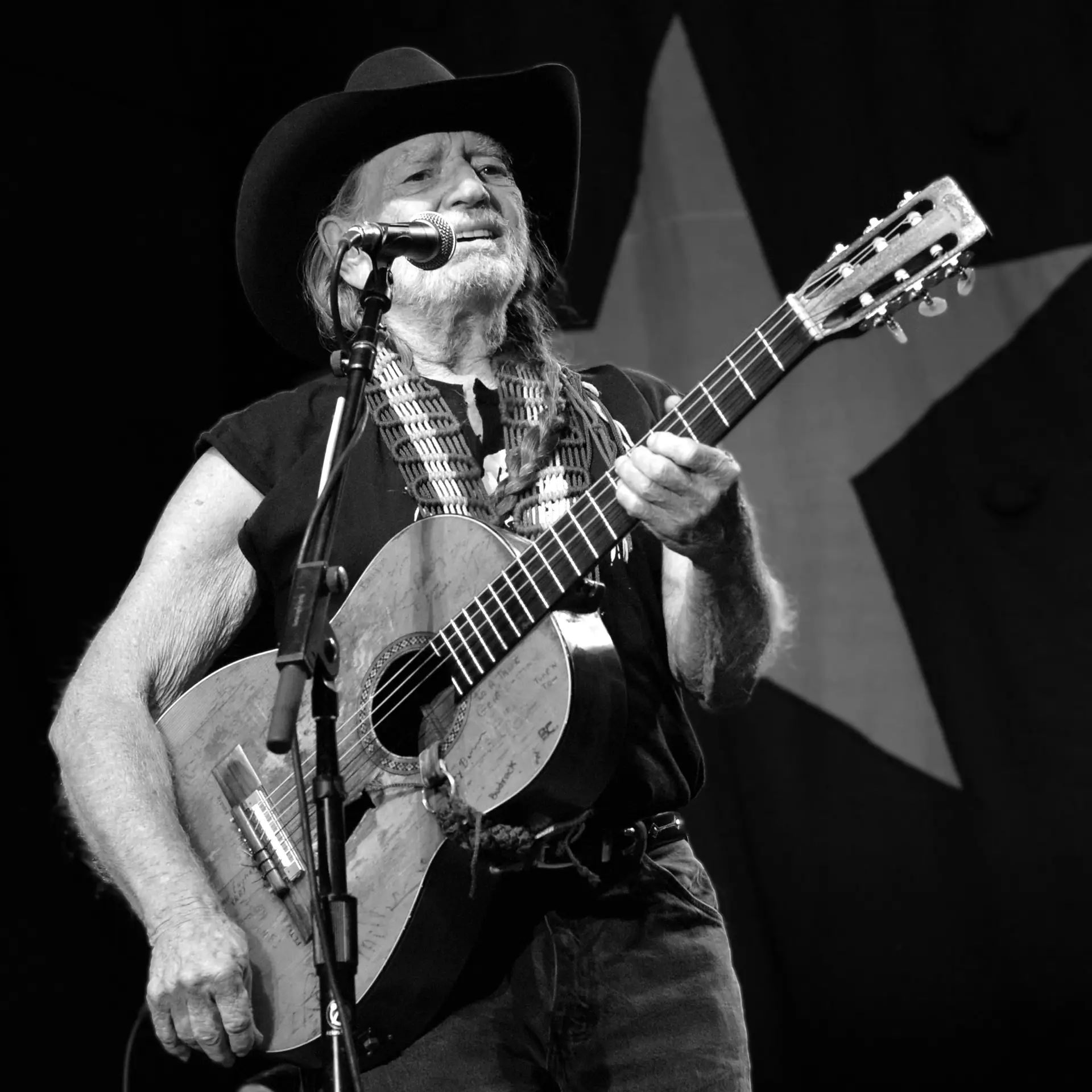 Willie Nelson performs live with his guitar Trigger in front of a Texas-star backdrop