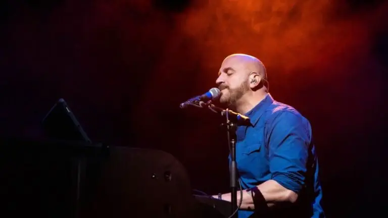 Mike DelGuidice performs at a keyboard under dramatic stage lighting at a live concert