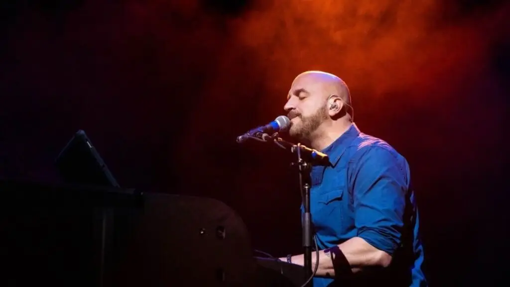 Mike DelGuidice performing live at piano on stage with dramatic red stage lighting