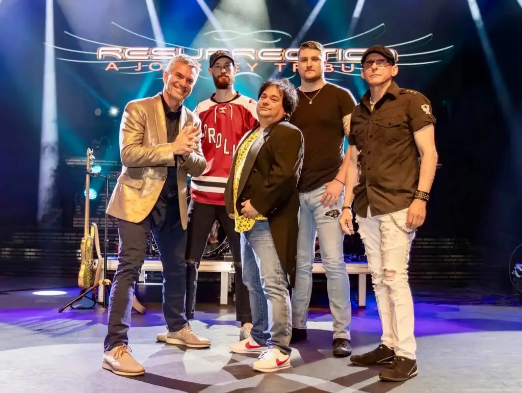 Resurrection: A Journey Tribute band members pose on stage in front of their logo backdrop