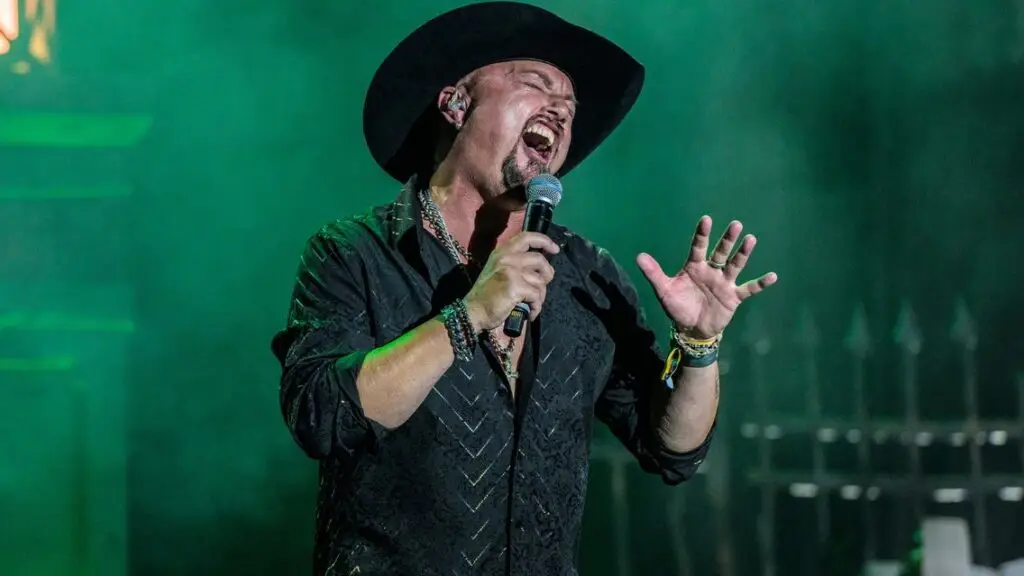 Geoff Tate performing live on stage, singing with microphone under green stage lighting
