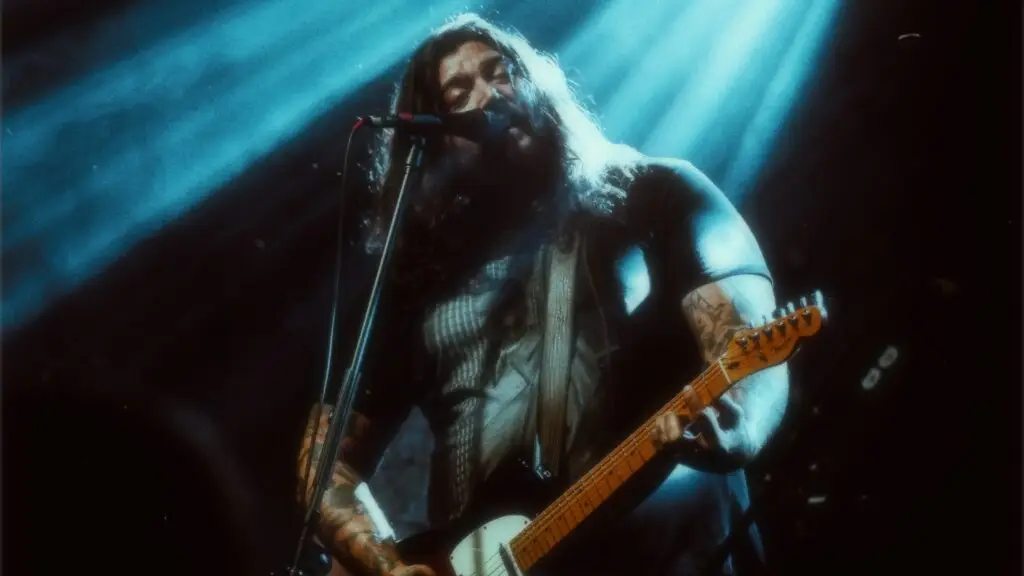 Amigo the Devil performs live on stage, singing and playing guitar under dramatic blue stage lights