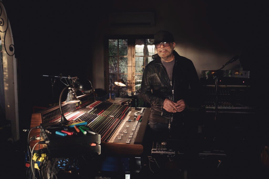 Daniel Lanois standing at mixing console in a dimly lit recording studio