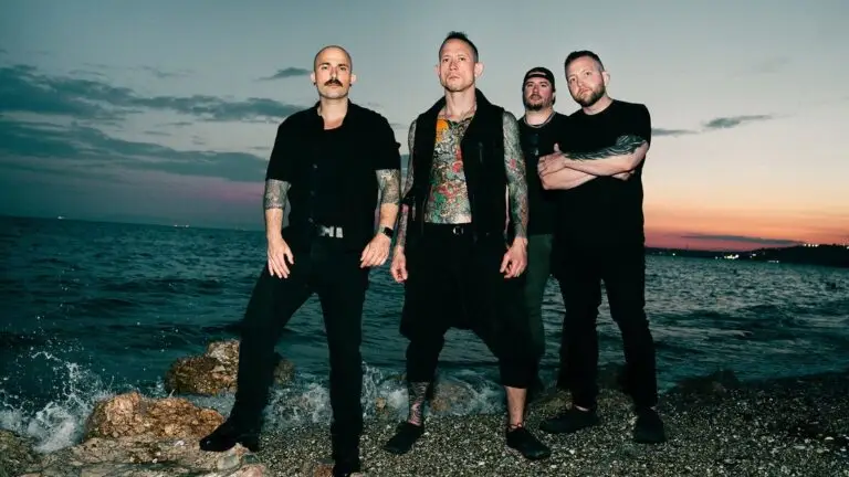 Trivium band members pose at rocky shoreline at sunset, official promotional photo for 2026 Crown in the Grave World Tour