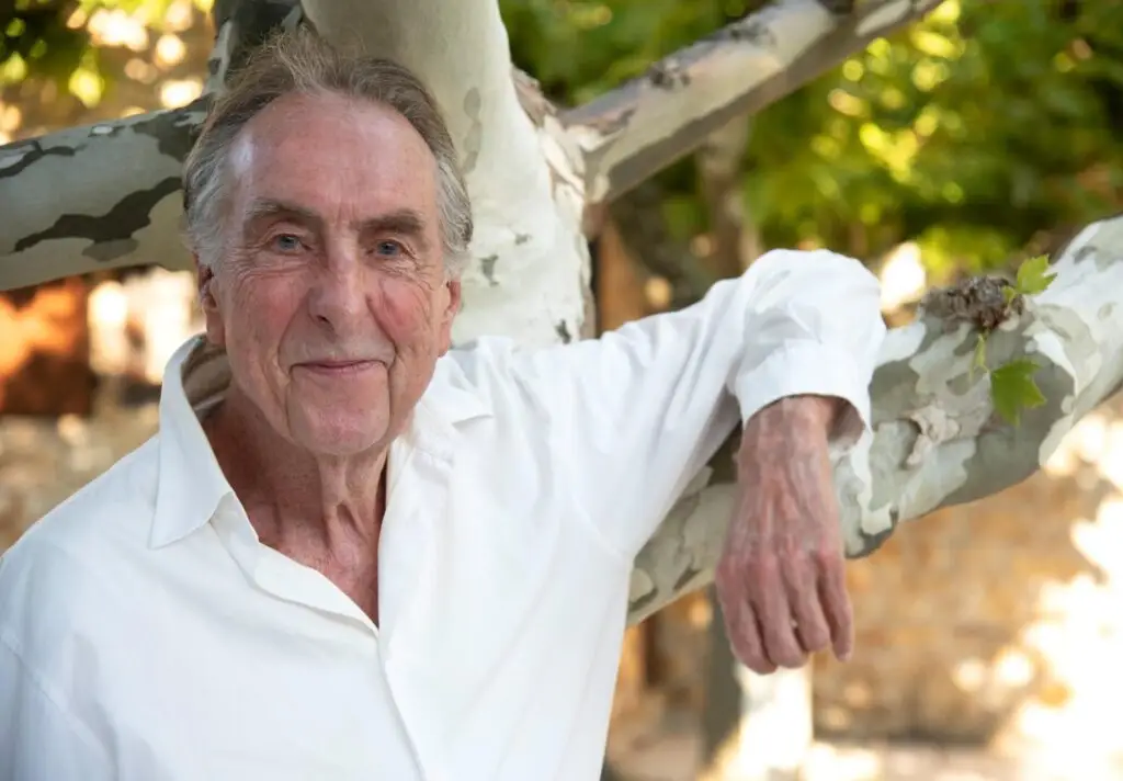 Eric Idle in a white shirt resting on a tree branch, official Idle in Provence tour photo