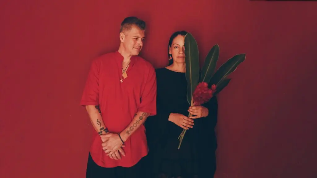 Rodrigo y Gabriela pose against a red background in an official press photo for their OurHome Tour