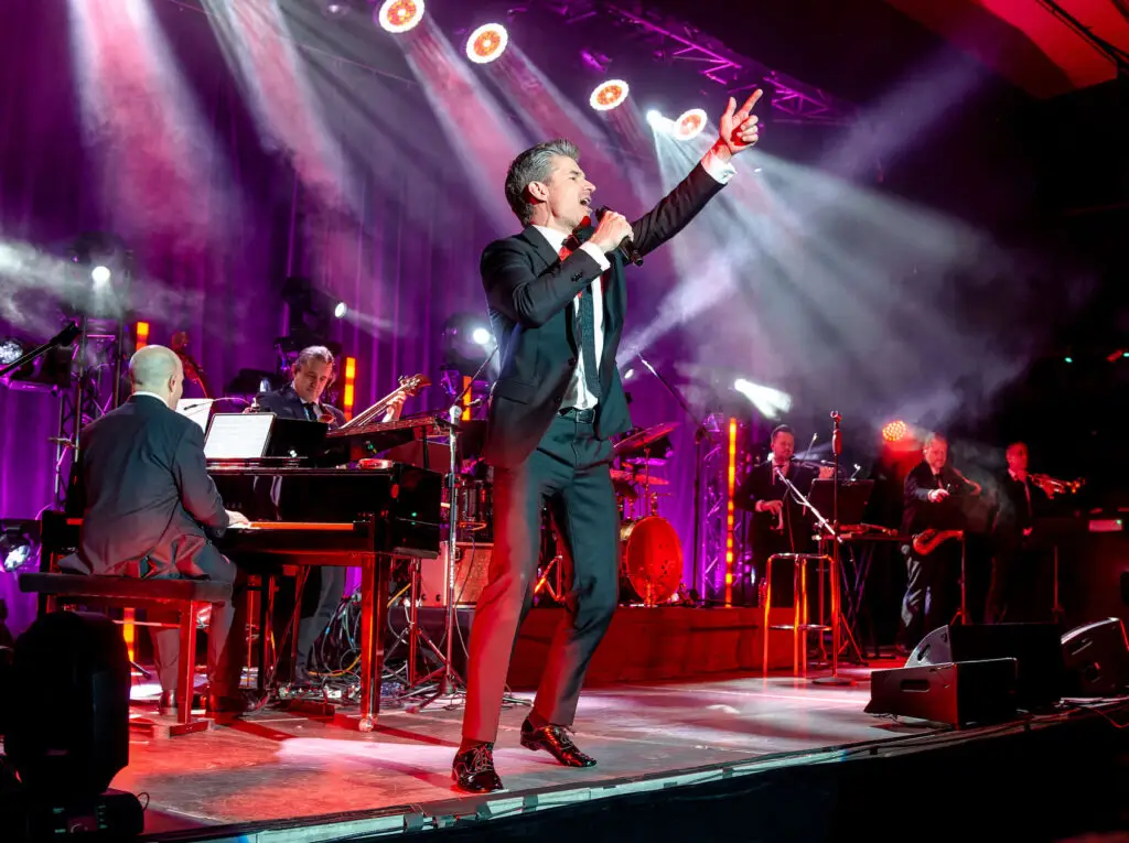 Matt Dusk singing live on stage with his full big band in dramatic concert lighting