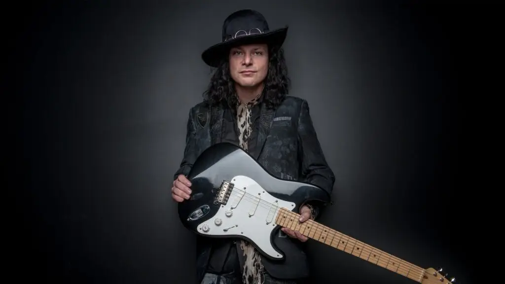 Anthony Gomes holds his Stratocaster guitar in a promotional photo for his 2026 world tour
