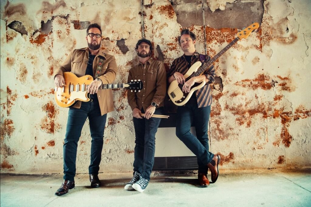 The Cold Stares blues-rock trio with guitars and bass against a rustic weathered wall