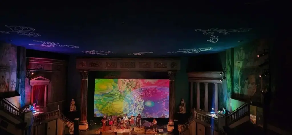 Wolfman Jack performs live on stage with a psychedelic projection screen backdrop in an ornate theater