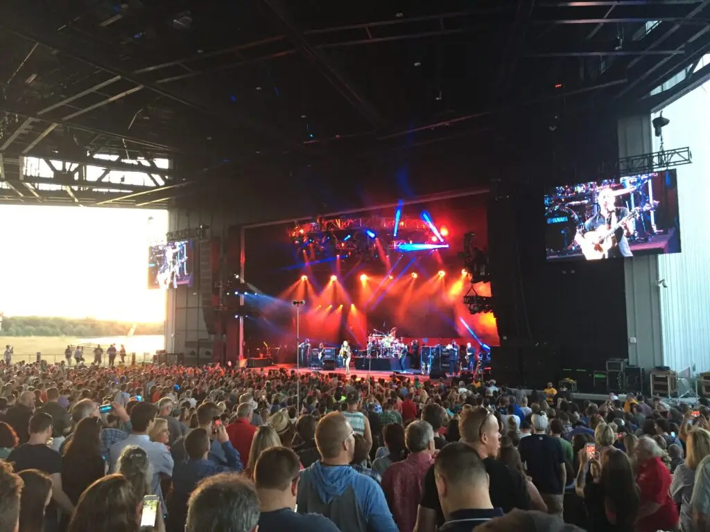 The covered stage and pavilion crowd at the Empower FCU Amphitheater during a concert, lawn and sunset visible at the open side