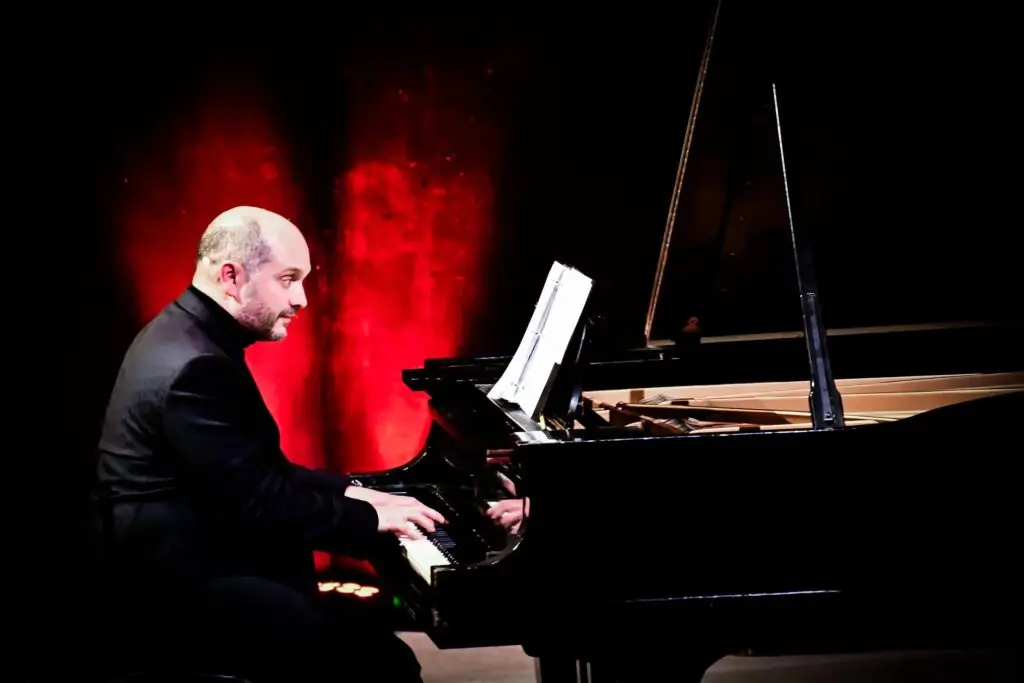 Mark Camilleri of JoyRide performing at grand piano, dramatic red stage lighting