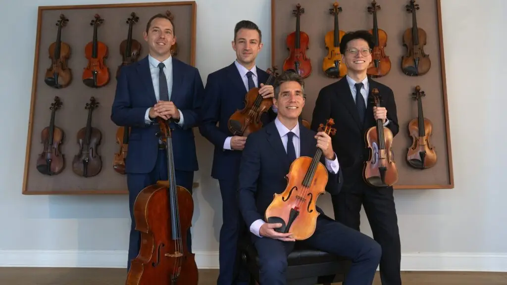 Escher String Quartet members in blue suits holding their instruments in a gallery setting