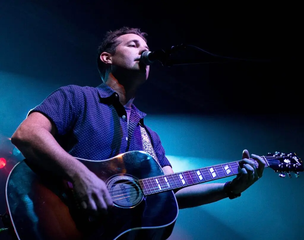 Nine Days performing acoustic live, vocalist singing with eyes closed at microphone with acoustic guitar
