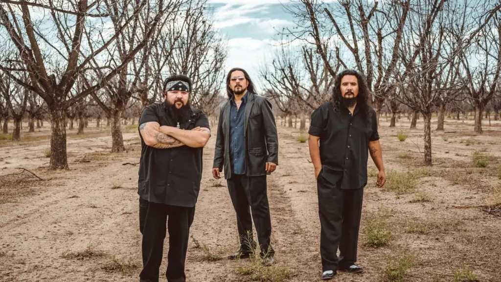 Los Lonely Boys — the Garza brothers pose in a sparse Texas orchard, Resurrection era press photo