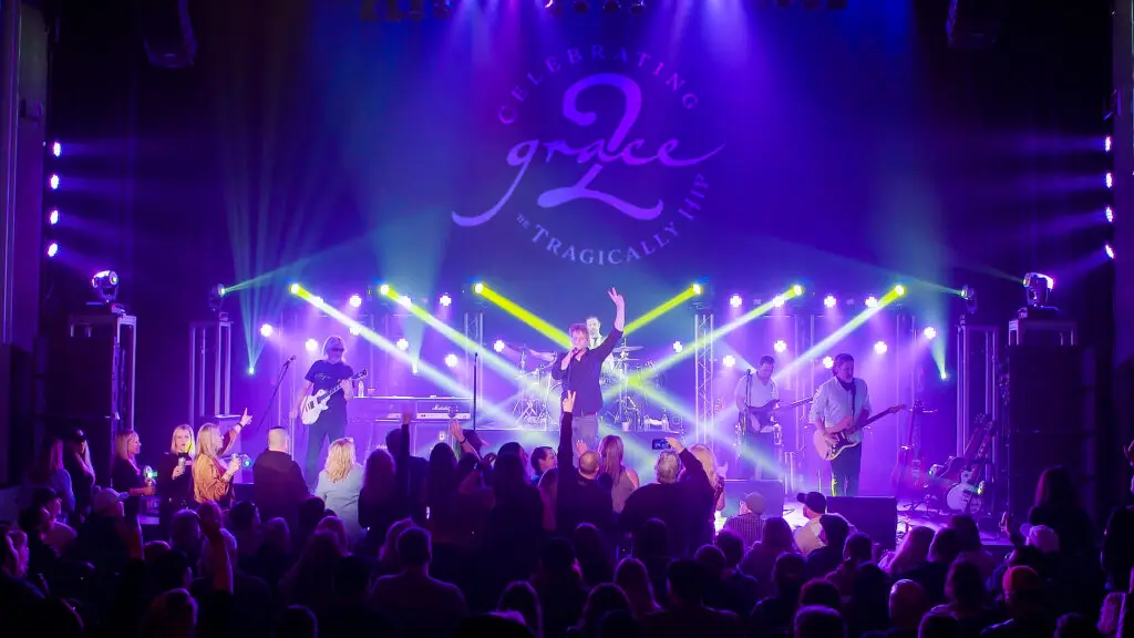 Grace 2 tribute band performing live on stage, vocalist arms raised, purple stage lighting