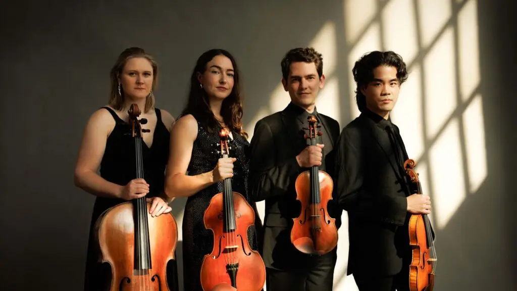 Callisto Quartet holding string instruments in black formalwear with dramatic window-light shadows