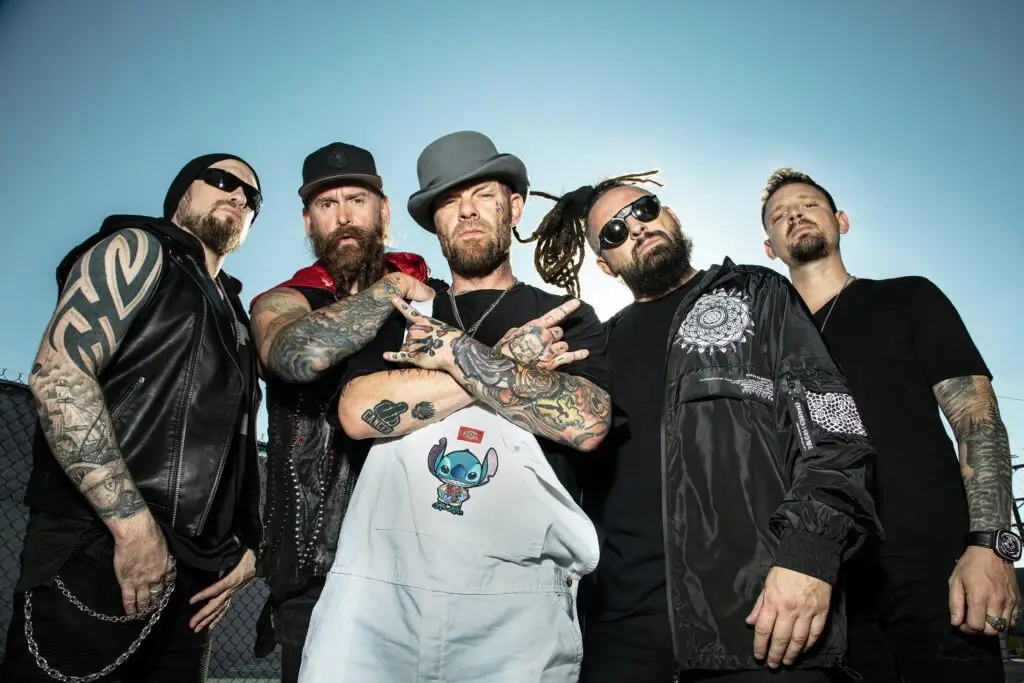 Five Finger Death Punch band members pose in low-angle outdoor shot against blue sky