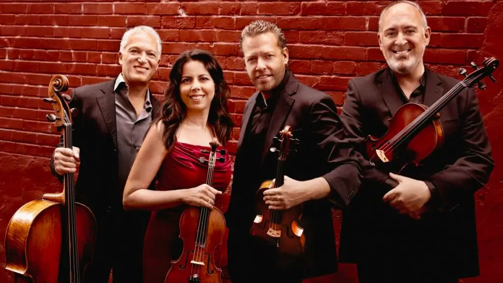 Pacifica Quartet with their string instruments against a red brick wall