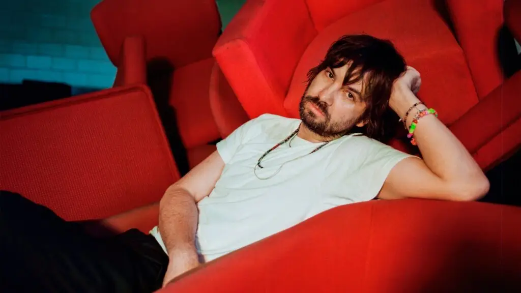 Kevin Parker of Tame Impala reclines in red cinema seats, Deadbeat Tour 2026 press photo