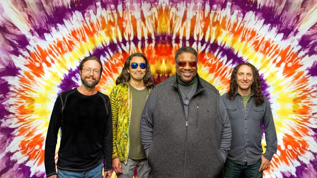 Melvin Seals and JGB band members posing in front of a colorful tie-dye backdrop