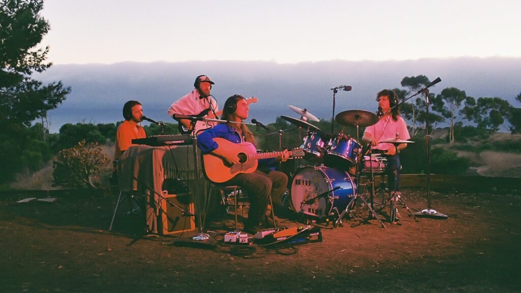 Improvement Movement performing live outdoors at dusk, four-piece band with keys, guitar, and drums