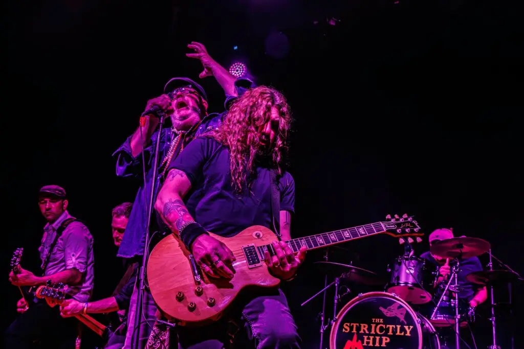 The Strictly Hip performing live, vocalist and guitarist front stage under purple stage lighting