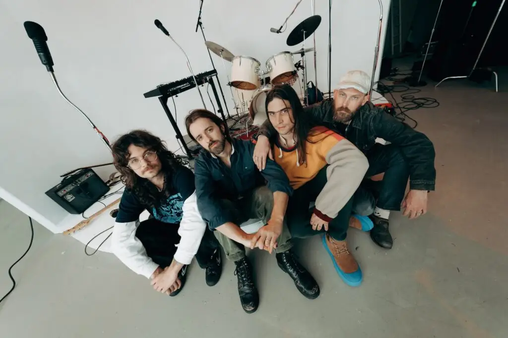 Improvement Movement quartet seated in a studio with drums and keyboards, 2025 press photo
