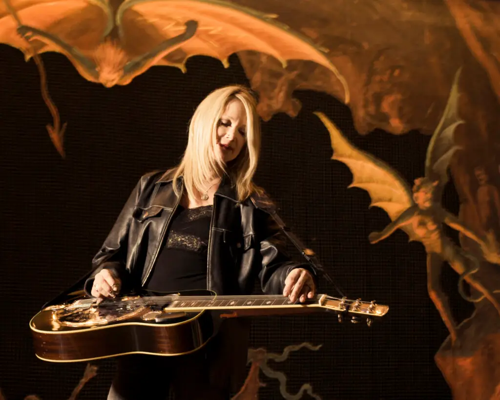 Cindy Cashdollar playing Dobro at an outdoor festival stage, blonde hair, black jacket