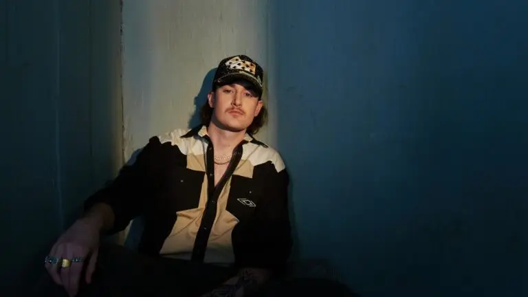 Austin Snell press photo, seated against blue wall in dramatic lighting, grunge country artist