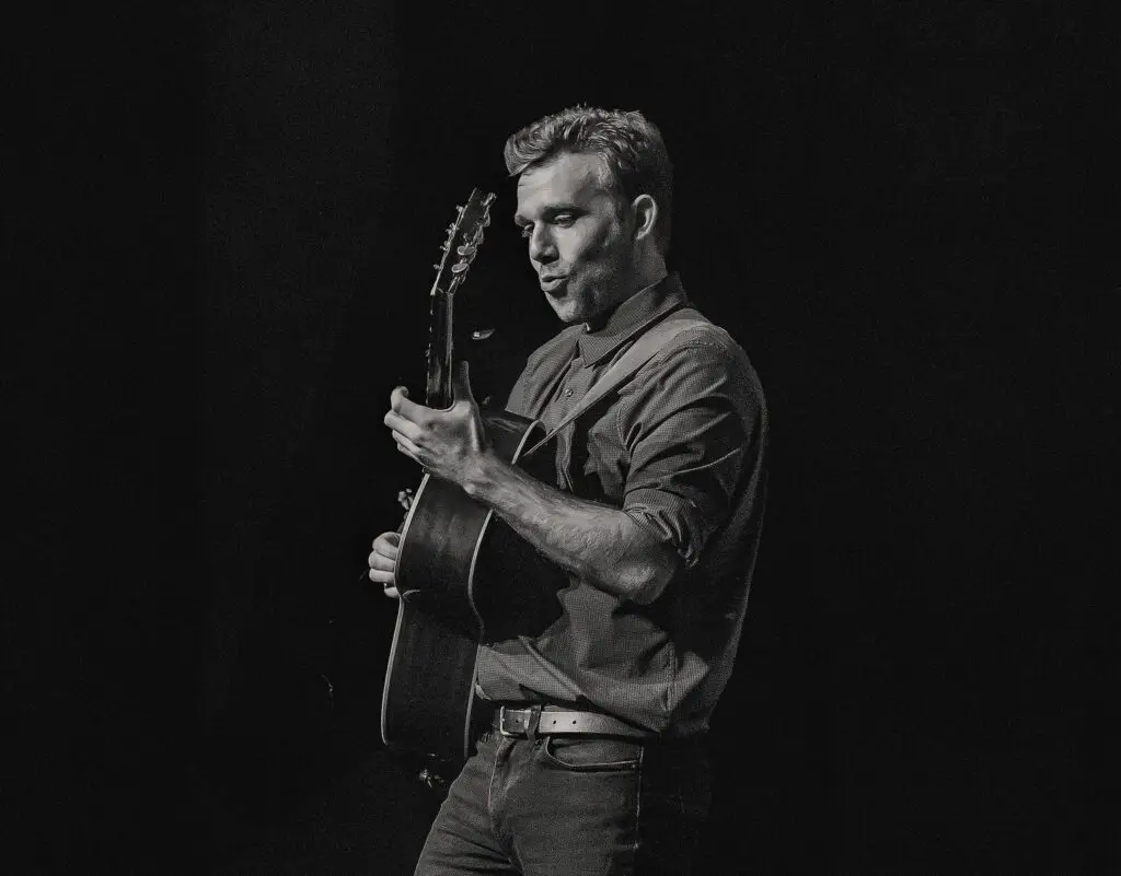 Gareth Pearson playing acoustic guitar on stage, live concert performance, side profile