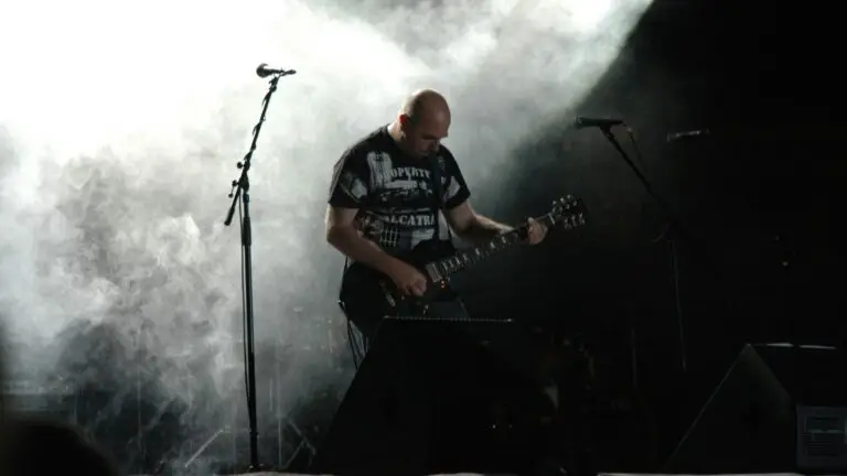 Vader guitarist Piotr Wiwczarek performing live on stage with dramatic backlighting and smoke effects