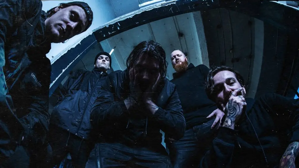 Distant band press photo, five members in dark industrial setting with dramatic blue lighting