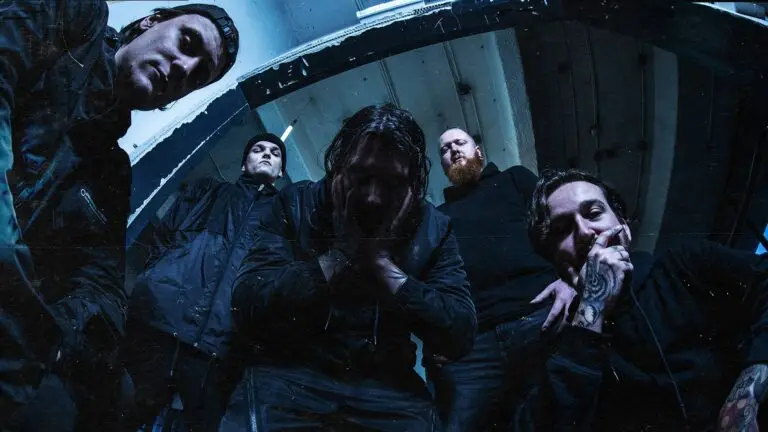 Distant band press photo, five members in dark industrial setting with dramatic blue lighting