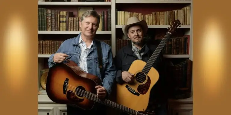 The Gibson Brothers, Eric and Leigh Gibson, holding acoustic guitars in front of a bookshelf